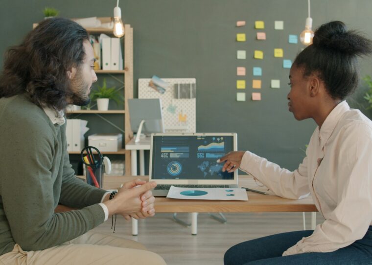 Zwei Kolleg:innen eines Commerce-Teams besprechen Produktdaten gemeinsam am Laptop in einem modernen Büro