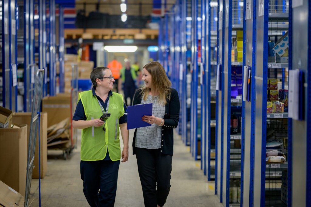 Two warehouse employees with a barcode scanner and clipboard in an organised storage aisle — structured product data as the basis for agent-ready commerce at apollon.
