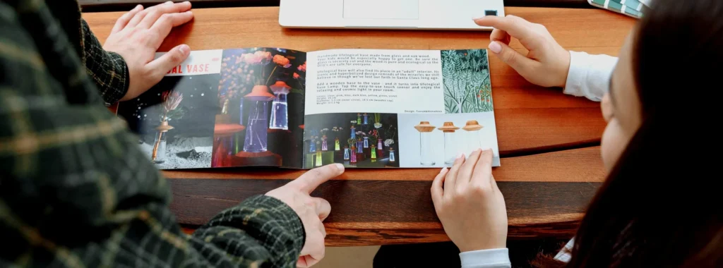 Two people reviewing a printed product catalogue next to a laptop — visual comparing flip catalogue and PDF