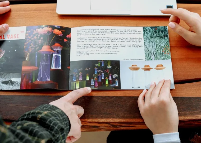Two people reviewing a printed product catalogue next to a laptop — visual comparing flip catalogue and PDF