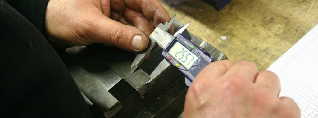Hands measuring a metal part with a digital caliper — visual for measurable product data quality