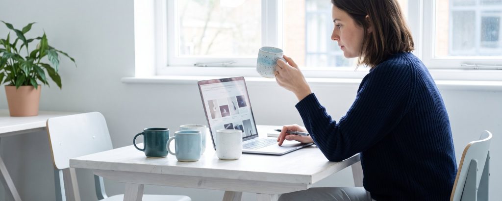 Texterin betrachtet eine Keramiktasse und schreibt die Produktbeschreibung