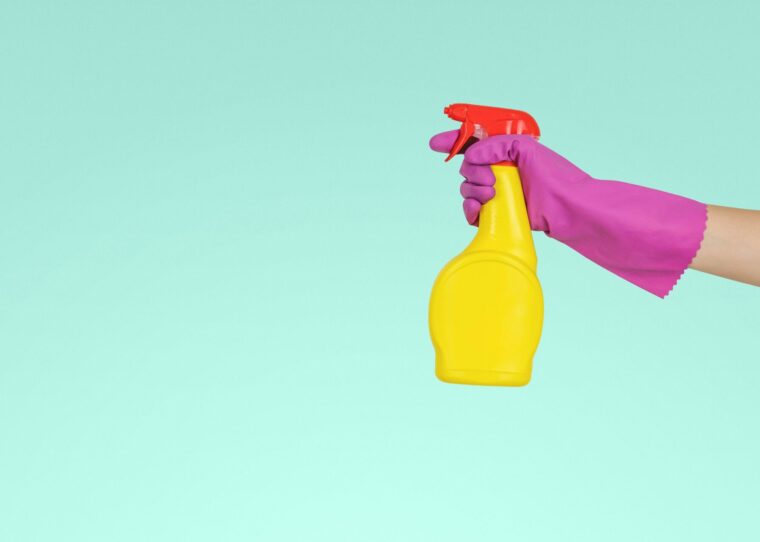 Gelbe Putzmittelflasche in der Hand einer Person mit einem lila Handschuh