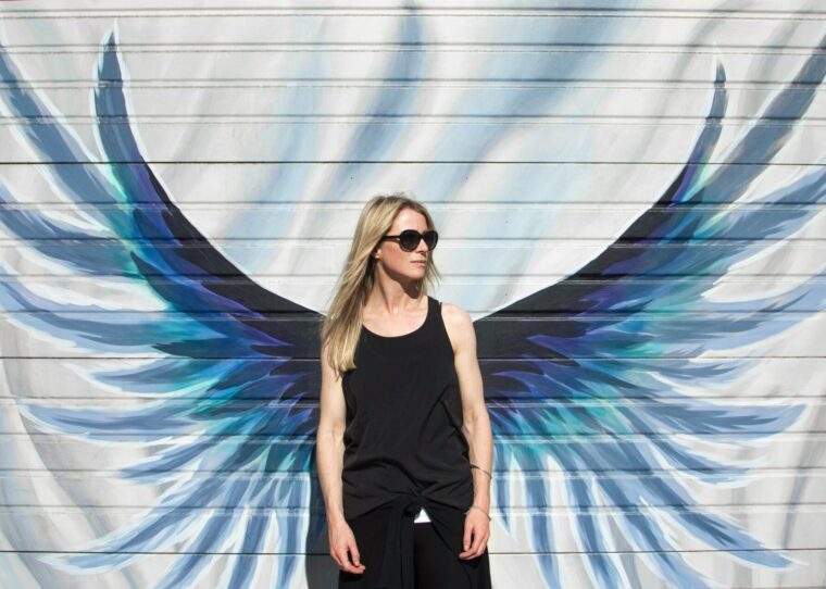 a woman standing in front of a wall with wings painted on it