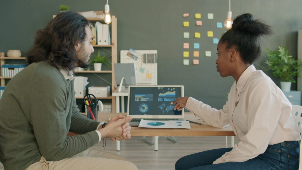 Two commerce team colleagues reviewing product data together on a laptop in a modern office