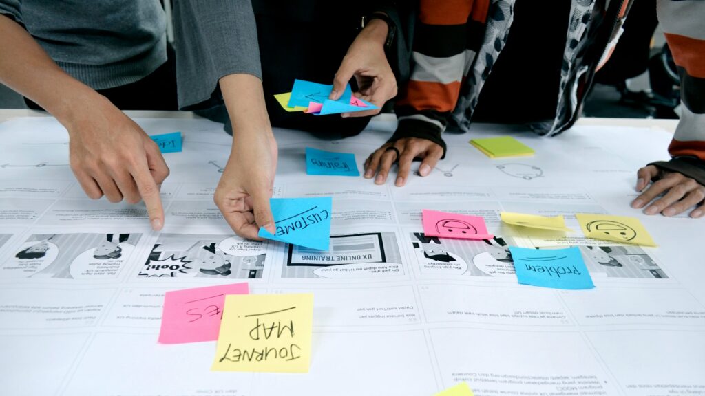 Four-person team in front of a wall of yellow and pink sticky-note columns, discussing the next step